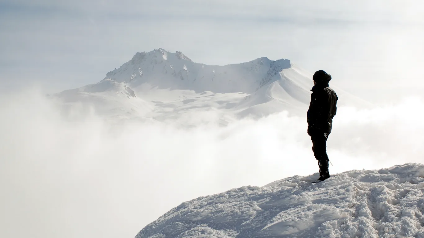 A climber on a snowy summit looking toward the peak ahead